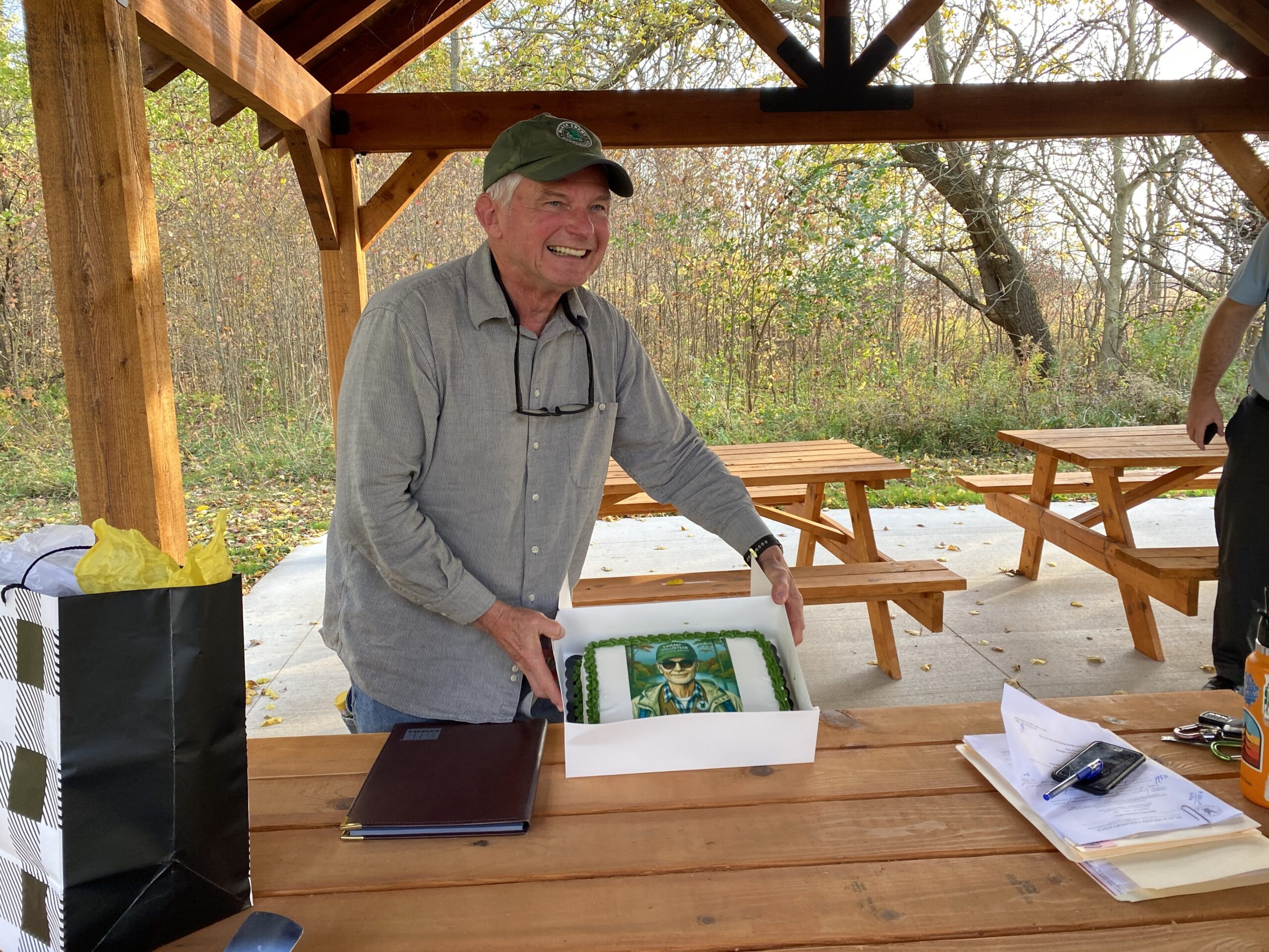 Volunteer monitor, Rick Bryan, smiling as he holds up a cake celebrating his 15 years as a volunteer